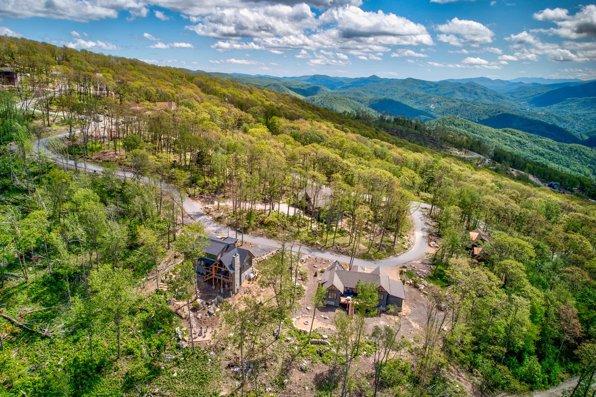 This image captures the main residence set against a dramatic mountain range, with a winding road leading through the surrounding trees. The scene embodies the gateway to outdoor adventure, suggesting immediate access to hiking and exploration in the natural landscape.