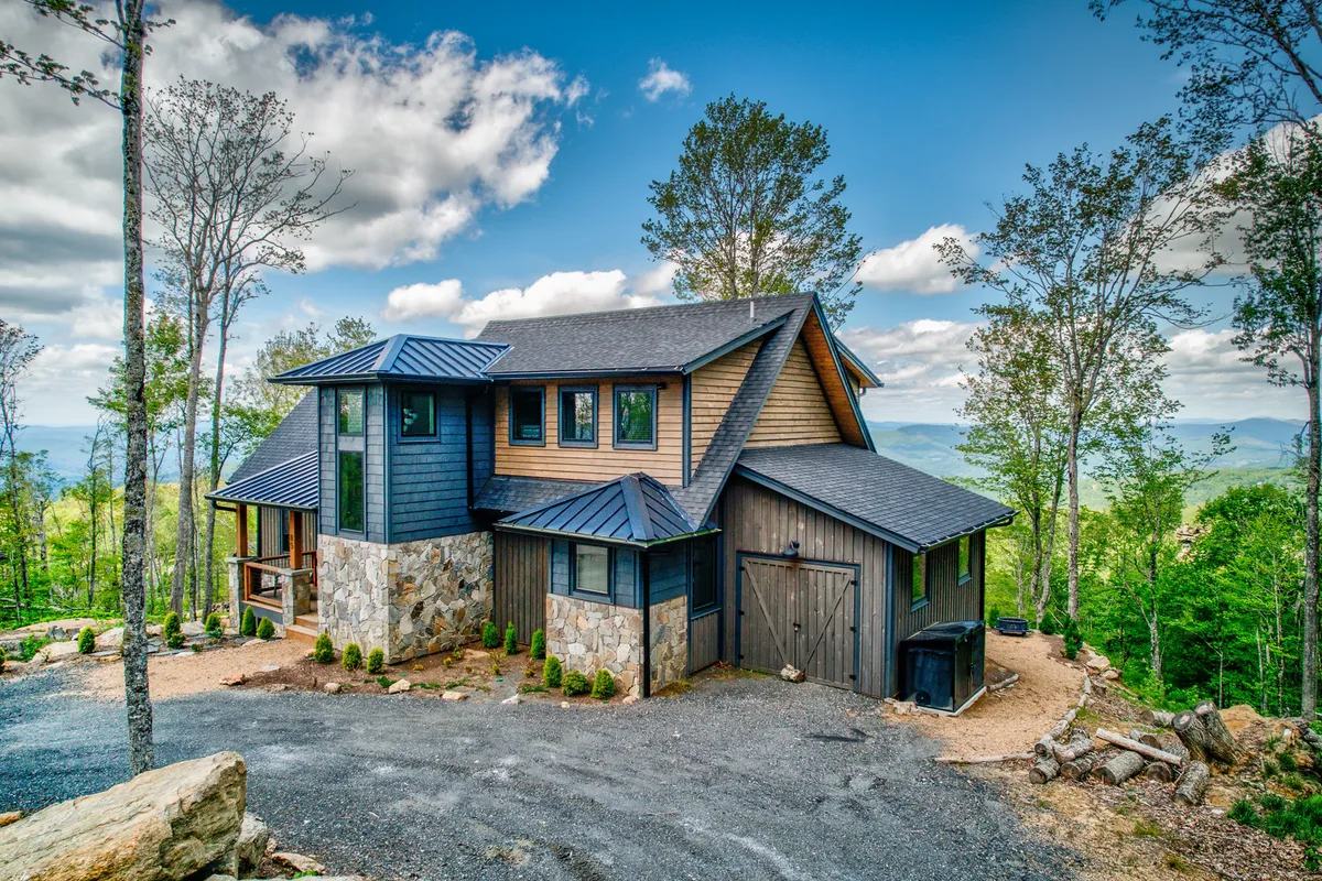 This exterior image showcases the modern architecture of the Eagles Nest community home, surrounded by serene trees and a spacious, open area perfect for dogs to roam. The porch offers panoramic views of the mountain setting, inviting relaxation and outdoor gatherings.