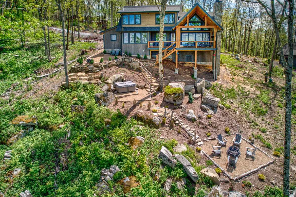 A close-up look at the wooden deck with a bubbling hot tub, adjacent fire pit area, and natural stone landscaping. The image emphasizes both the spa-like retreat of the hot tub and the social warmth of the fire pit, surrounded by tranquil nature.