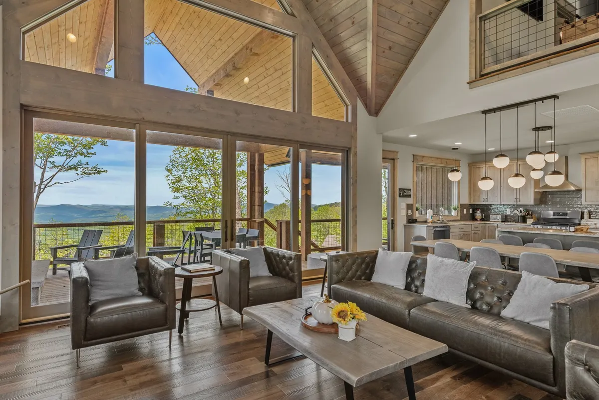 A spacious living room with stylish leather sofas, a chic dining area with modern lighting, and expansive windows looking out to the mountains. The scene exudes warmth and invites relaxation, conversation, and shared meals.