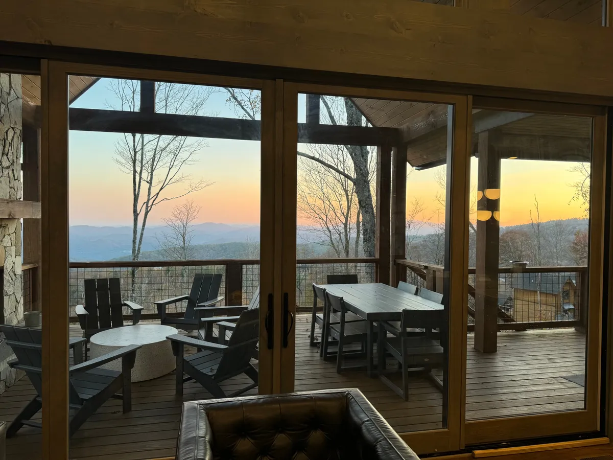 This image captures an outdoor seating area with a dining table set against a stunning sunset backdrop, creating a peaceful and inviting atmosphere for relaxing with friends. The view from the seating area opens onto rolling mountains, perfectly encapsulating the Blue Ridge setting.