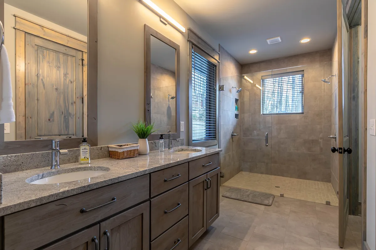 A serene, contemporary bathroom with a double sink vanity, a spacious walk-in shower, and natural light pouring through a window. The layout is generous and accessible, perfect for pampering and ease of use for all guests.