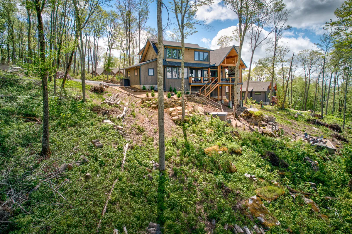 A wide view of the house shows the large deck area and landscaped yard, with ample space for outdoor play, relaxation, and family gatherings. The surrounding trees and inviting atmosphere hint at the possibilities for games, nature walks, and group activities right outside the door.
